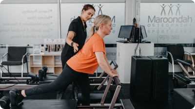 Practitioner helping woman in a Pilates Class